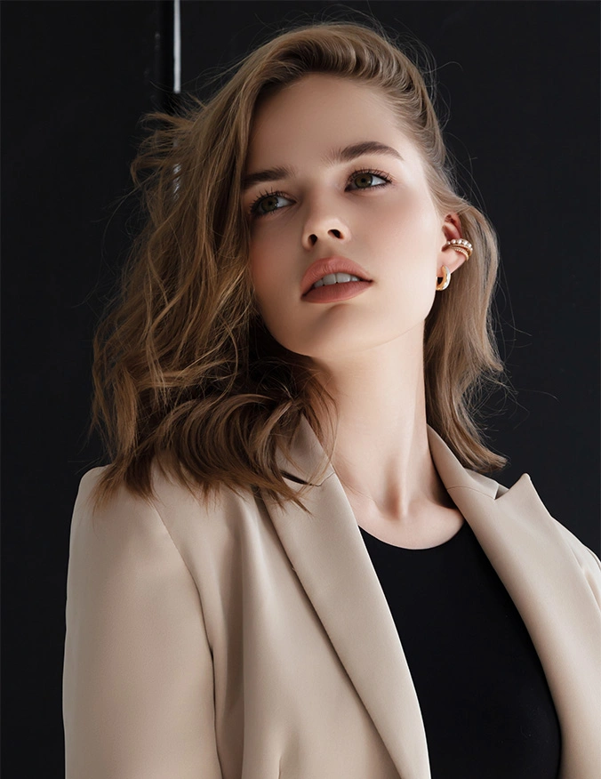 A close-up portrait of a woman with wavy brown hair looking upward and to the side, wearing a tan blazer over a black top with gold hoop earrings. - Genetic testing in Draper, UT