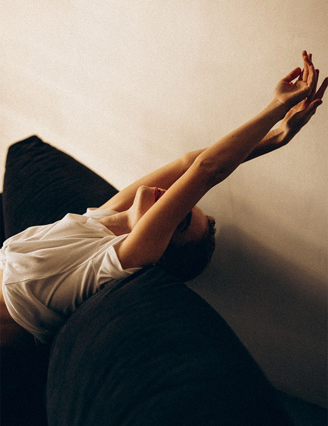 An artistic, high-angle shot of a person reclining back on a dark surface with their arms extended upward toward a warm, neutral-toned wall. - Upper body lift in Draper, UT